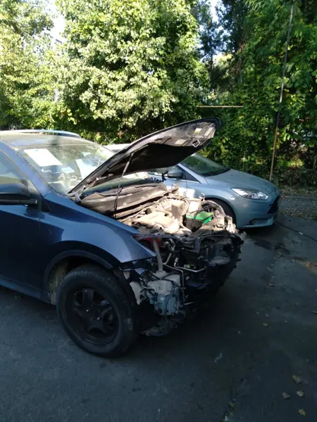 Dark car with an open bonnet and dismantled front end near the workshop