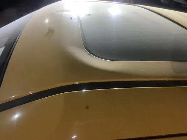 Roof of a gold-coloured car with damage near the sunroof